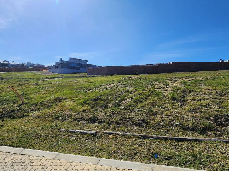 A vacant residential plot featuring a gentle slope, paved street frontage, and existing boundary walling in a developed estate setting.