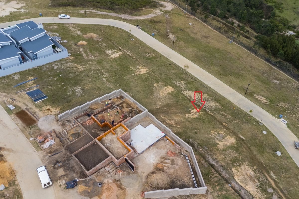 Aerial view of a residential vacant land plot showing ongoing construction of building foundations and perimeter walls within a developed estate.