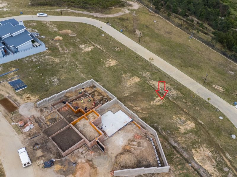 Aerial view of a residential vacant land plot showing ongoing construction of building foundations and perimeter walls within a developed estate.