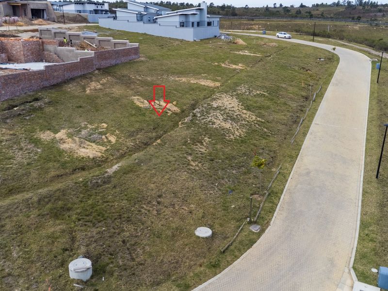 Aerial view of a vacant residential plot in a developing estate, featuring paved road access and surrounding infrastructure.