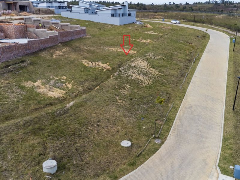 Aerial view of a vacant residential plot in a developing estate, featuring access to a paved road and existing infrastructure.
