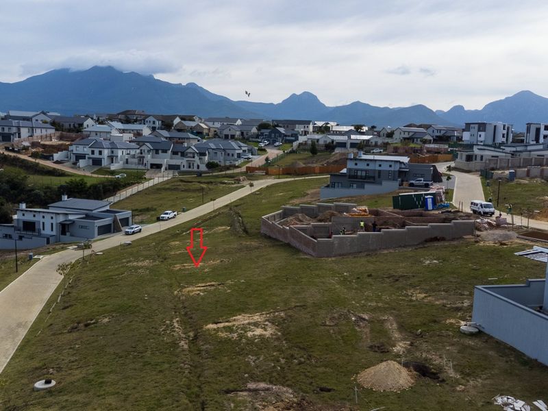 Aerial view of a vacant residential plot within a developed estate, featuring surrounding modern homes and mountain views.