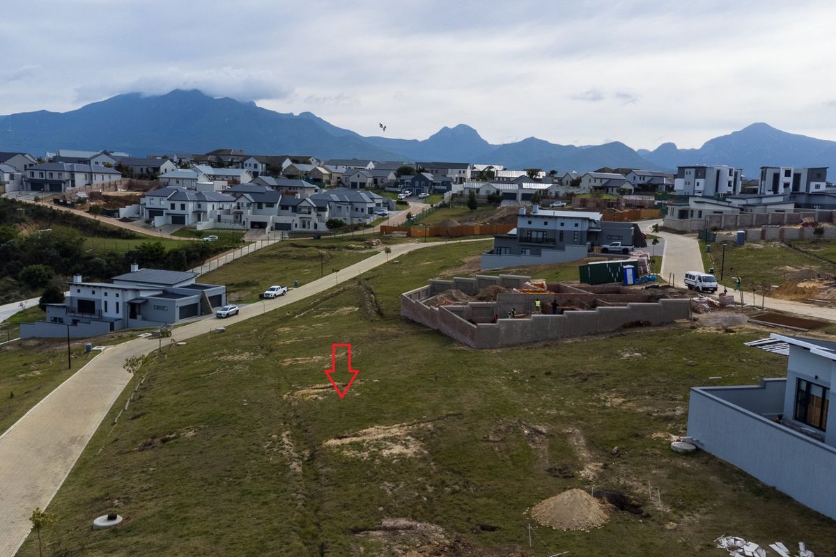 Aerial view of a vacant residential plot situated within a developed estate, featuring paved road access and scenic mountain views.