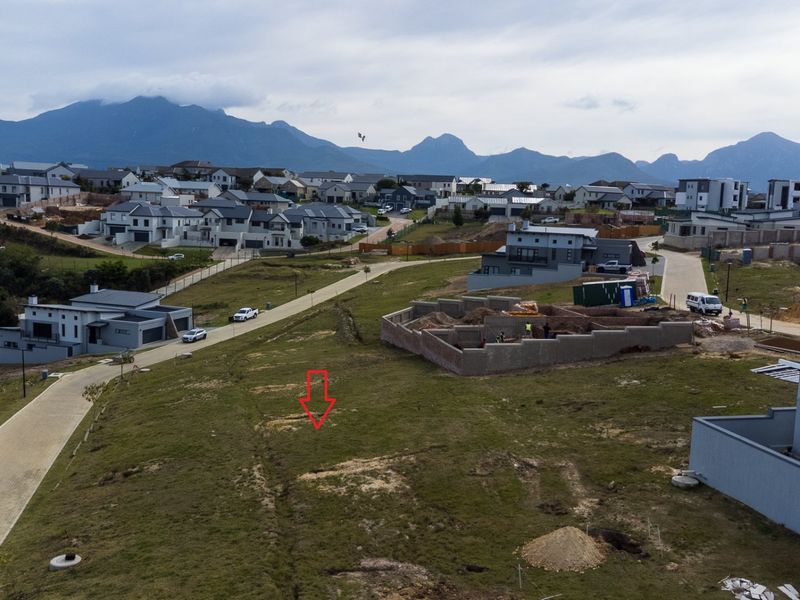 Aerial view of a vacant residential plot situated within a developed estate, featuring paved road access and scenic mountain views.
