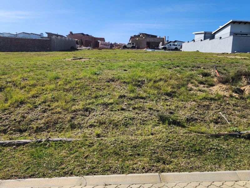A vacant residential plot of land featuring grass cover, bordered by boundary walls in a developing estate setting.