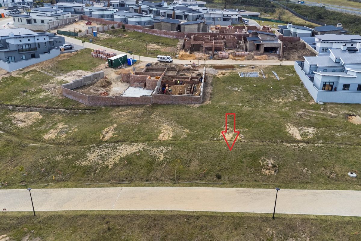 Aerial view of a vacant residential plot in a developing estate, featuring paved road access and surrounding construction activity.
