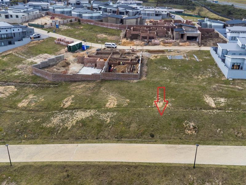 Aerial view of a vacant residential plot in a developing estate, featuring paved road access and surrounding construction activity.
