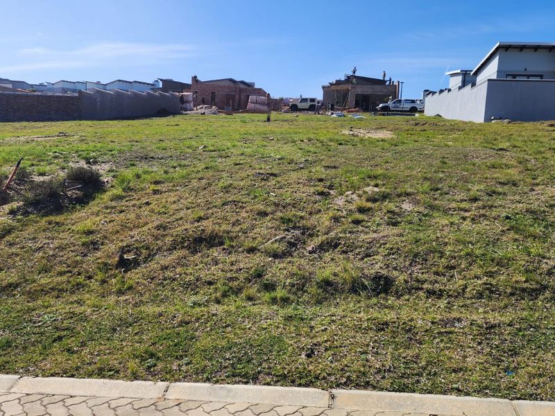 A vacant residential plot of land situated in a developing estate, featuring established boundary walls and surrounding construction activity.
