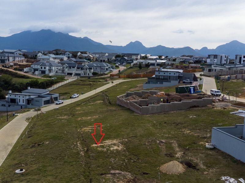 Aerial view of a vacant residential plot within a developed estate, featuring mountain views and access to paved estate roads.