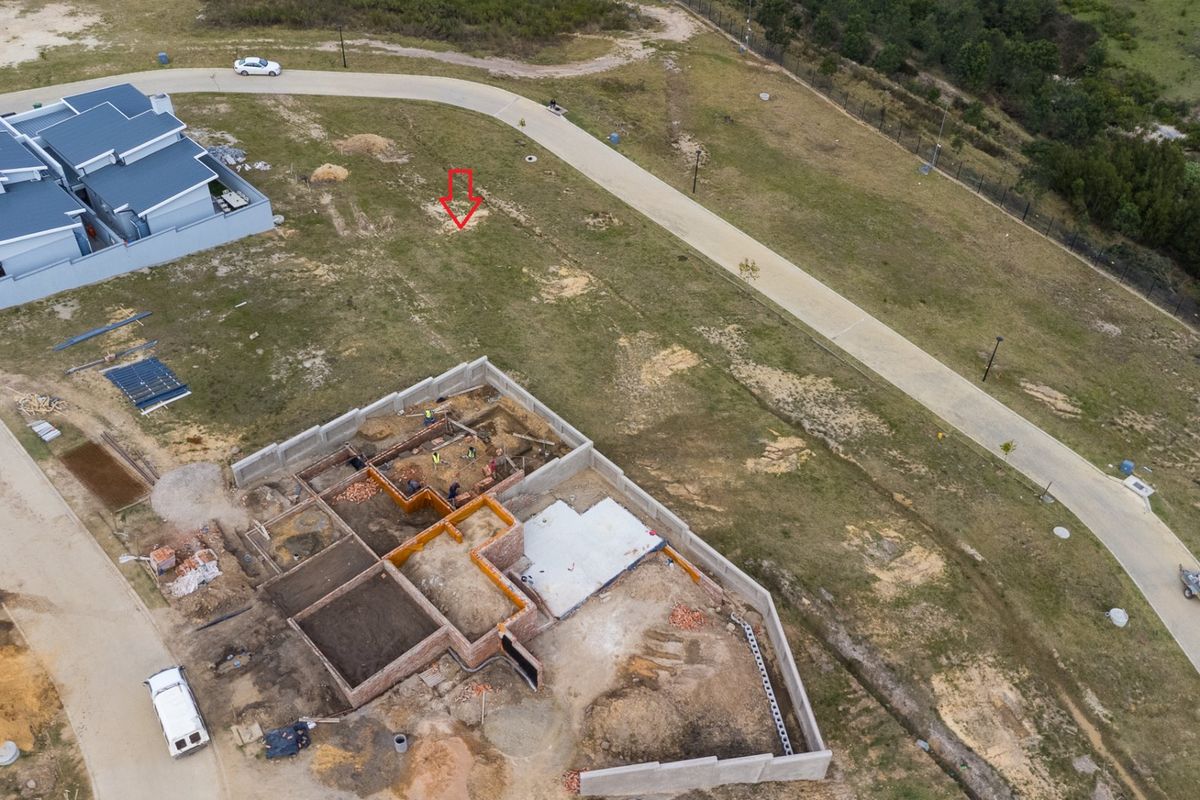 Aerial view of a residential vacant land plot showing ongoing construction of building foundations and masonry walls within a developed estate.