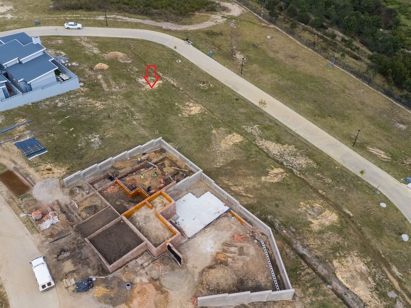 Aerial view of a residential vacant land plot showing ongoing construction of building foundations and masonry walls within a developed estate.