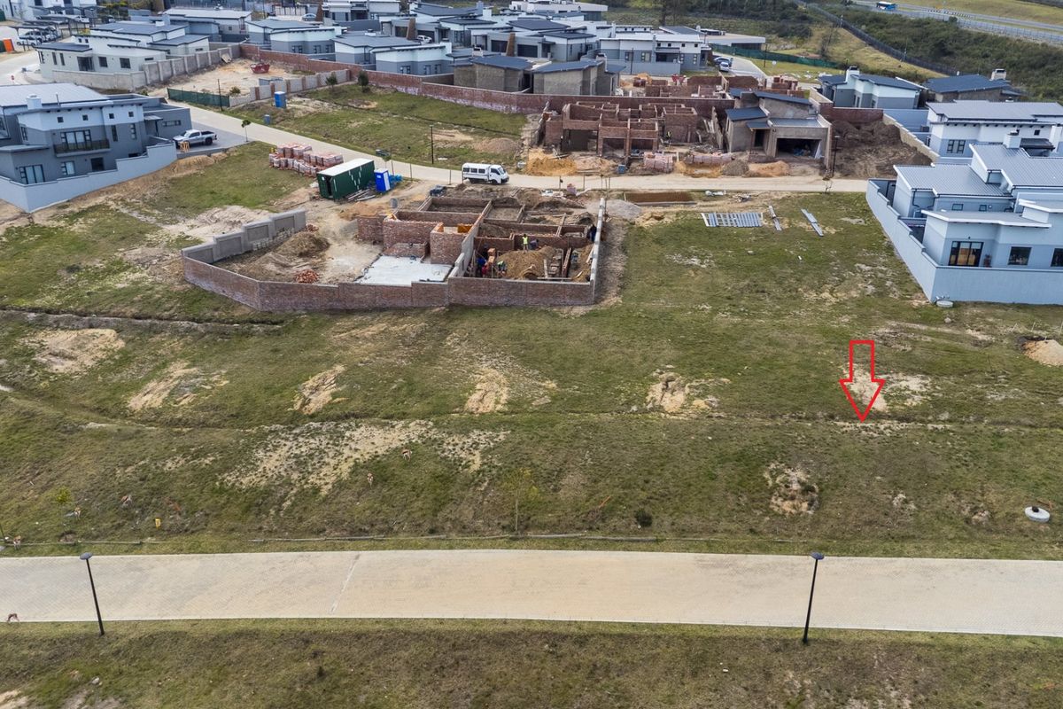 Aerial view of a vacant residential plot in a developing estate, featuring paved road access and surrounding construction activity.