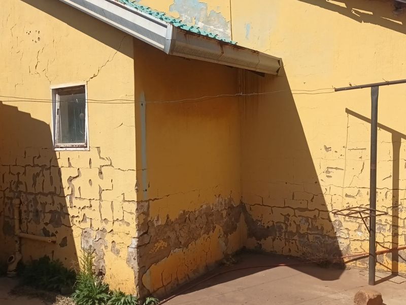 Rear exterior view of the property showing significant wear to the wall plaster and paintwork, requiring maintenance and repair.