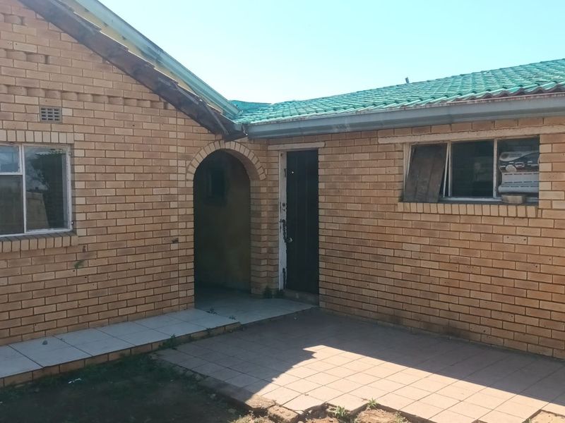 Rear exterior view of a face brick house featuring a tiled patio area, arched entrance, and green roof tiles requiring maintenance.