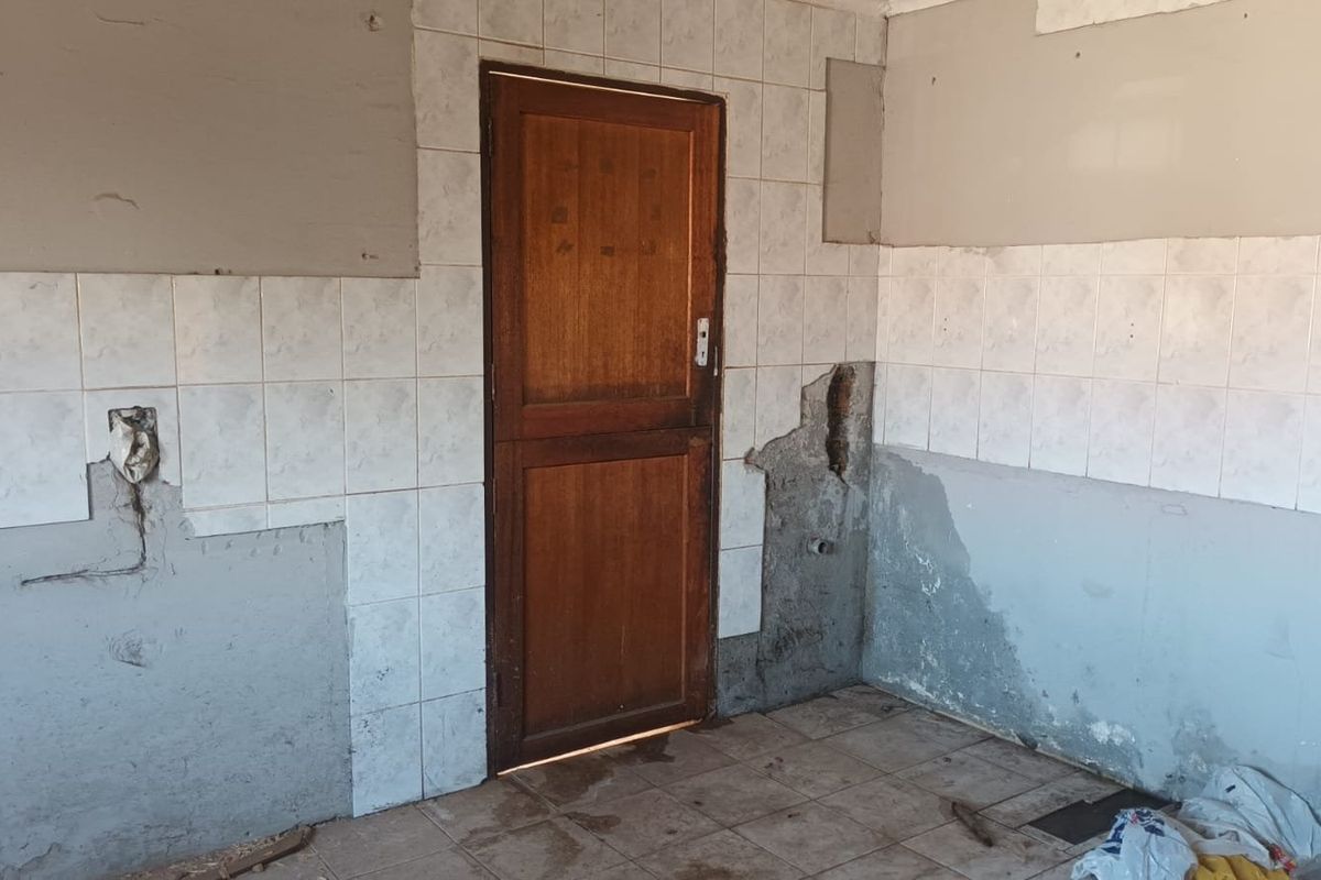 A kitchen area in need of renovation, featuring tiled walls and flooring with significant damage to the wall plaster and missing tile sections.