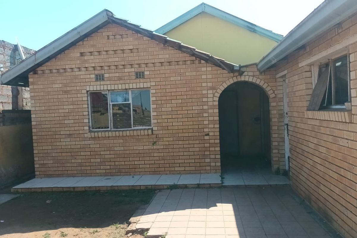 Rear exterior view of a face brick house featuring an arched entrance, tiled patio area, and gable roof structure.