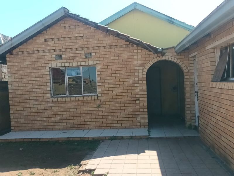 Rear exterior view of a face brick house featuring an arched entrance, tiled patio area, and gable roof structure.
