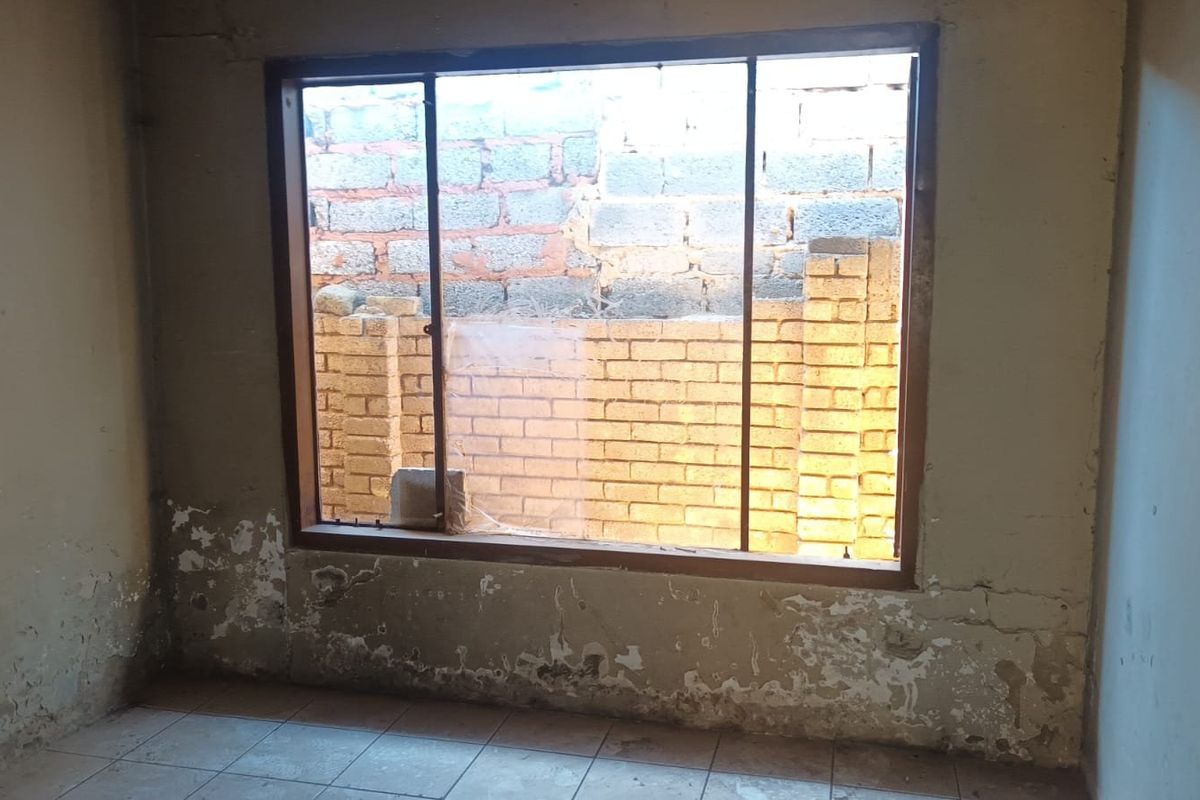 An empty bedroom featuring tiled flooring and a large window, currently requiring significant wall repairs and cosmetic renovation to restore the space.