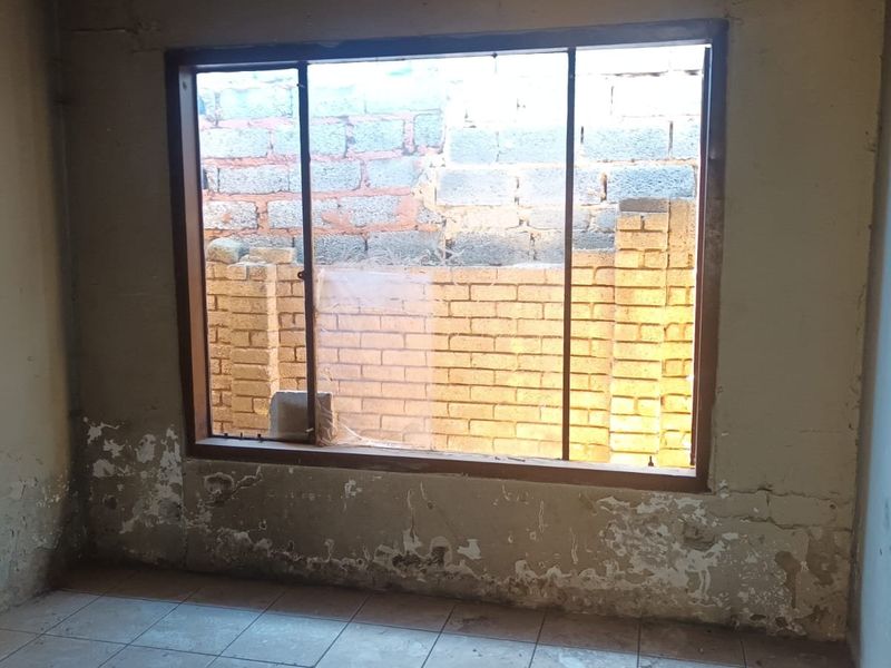 An empty bedroom featuring tiled flooring and a large window, currently requiring significant wall repairs and cosmetic renovation to restore the space.