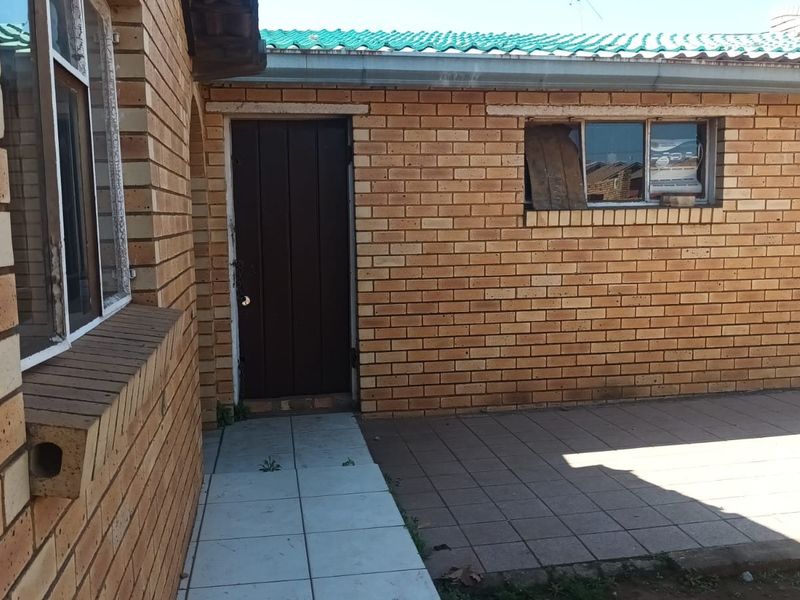 Rear exterior view of the property featuring a face brick facade, tiled patio area, and a timber entrance door with a damaged window.