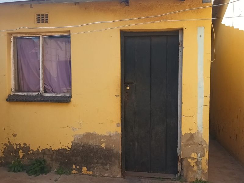 Rear exterior view of the property showing a yellow painted wall with visible plaster damage and peeling paint around the base.