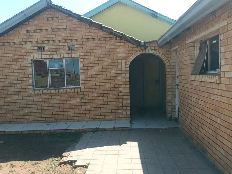 Rear exterior view of a face brick house featuring an arched entryway, tiled patio area, and pitched roof structure.