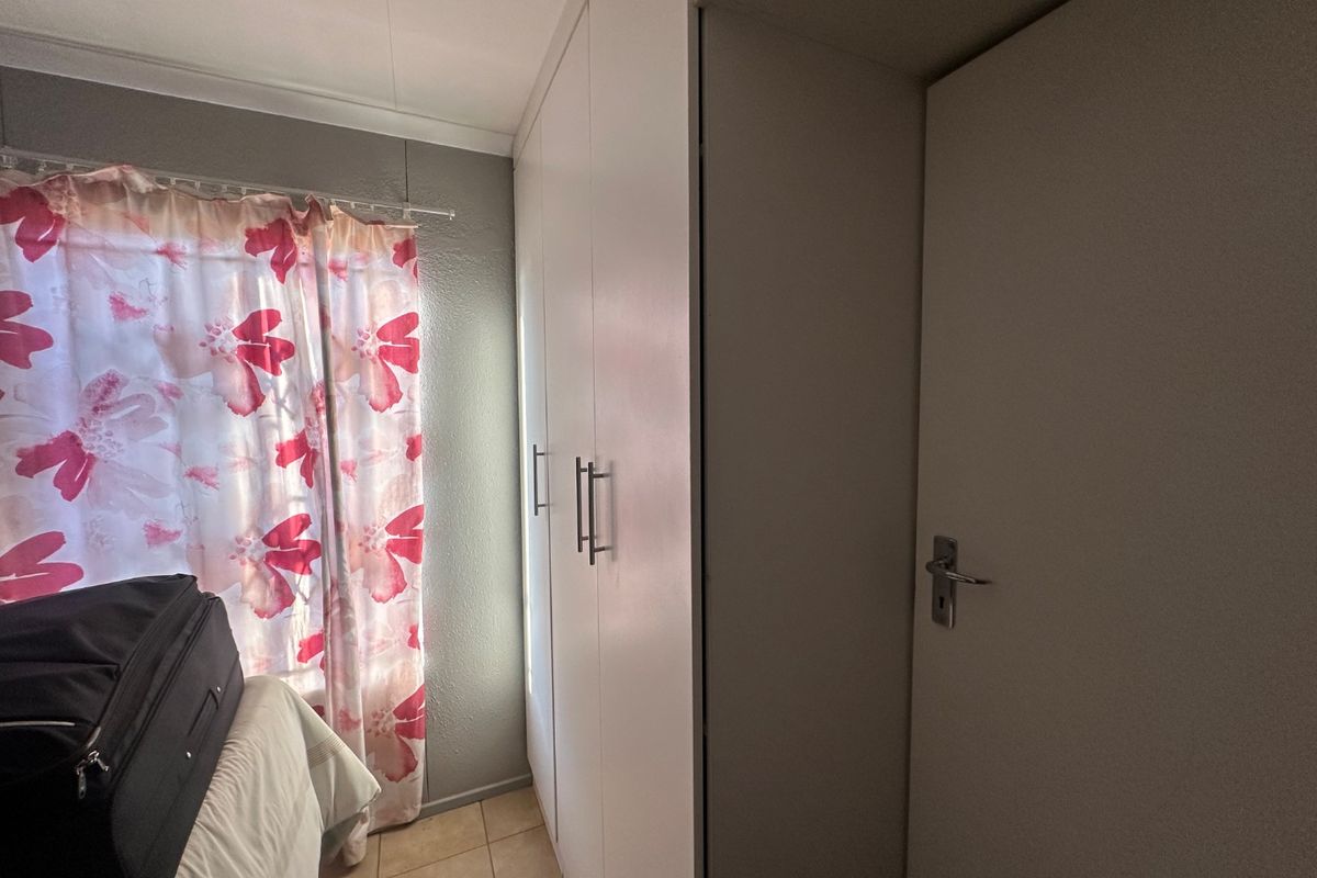 A bedroom featuring built-in cupboards, tiled flooring, and a standard internal door, providing functional storage and access.