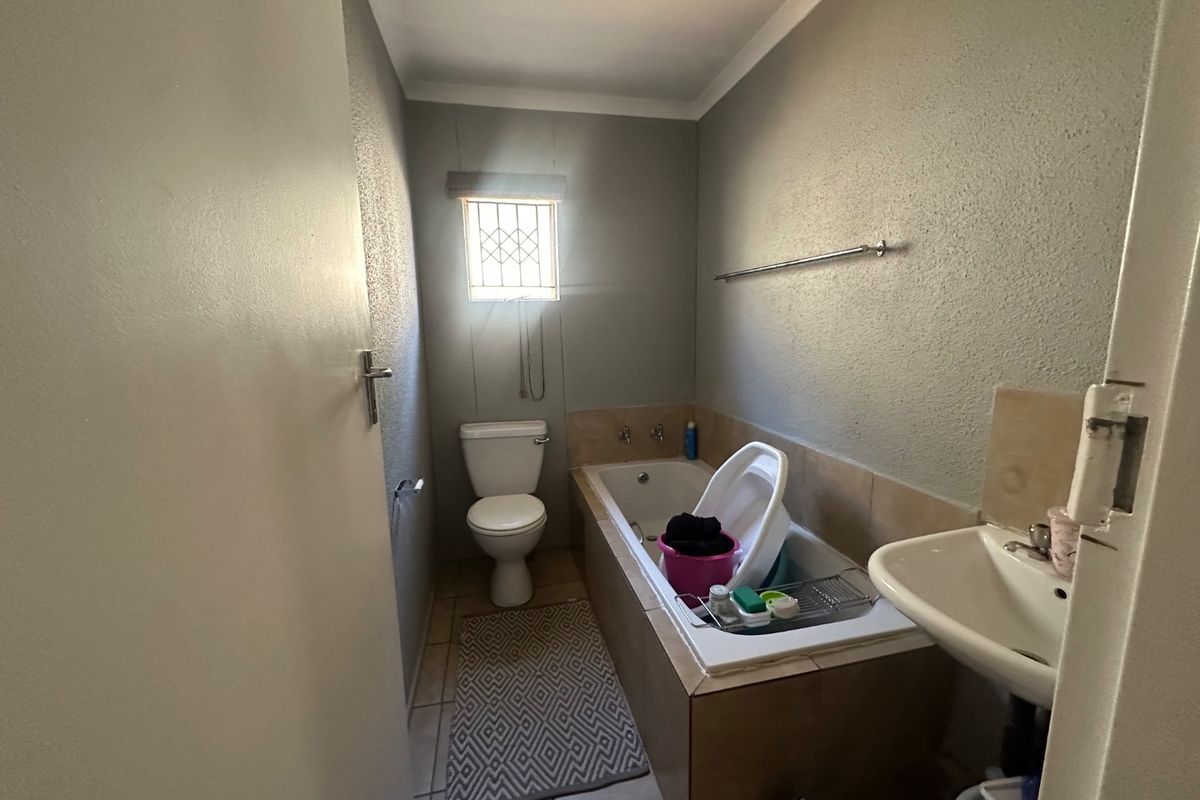 A functional bathroom featuring a bathtub, toilet, and wall-mounted washbasin, with neutral wall finishes and a security-fitted window.