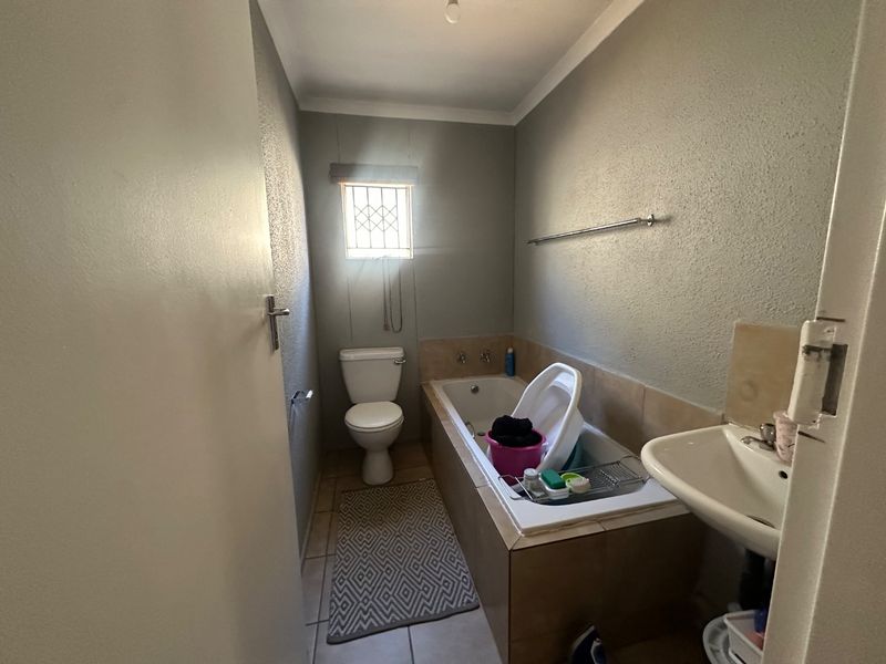 A functional bathroom featuring a bathtub, toilet, and wall-mounted washbasin, with neutral wall finishes and a security-fitted window.