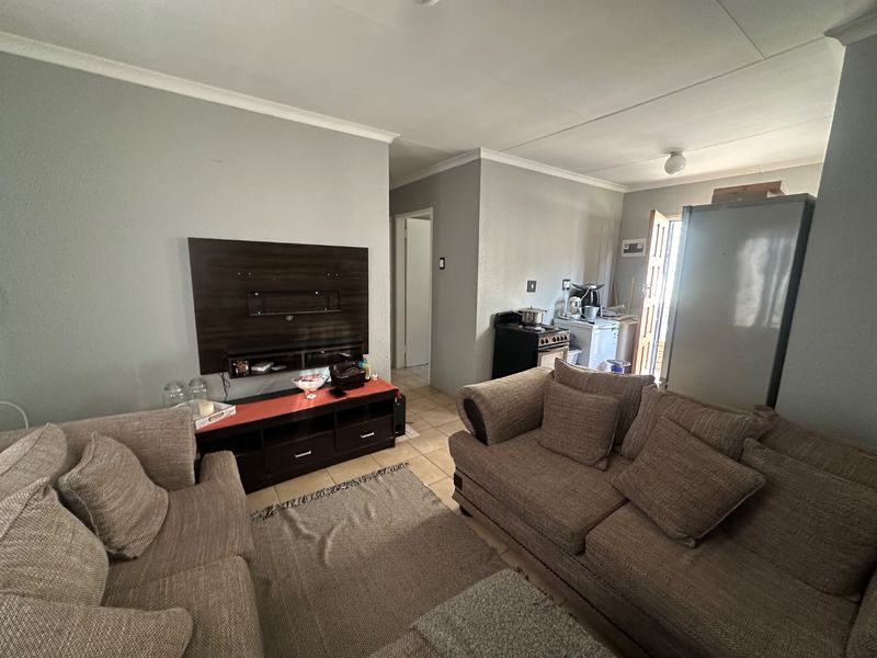 Open plan living area featuring tiled flooring and coved ceilings, with an integrated kitchen space visible in the background.