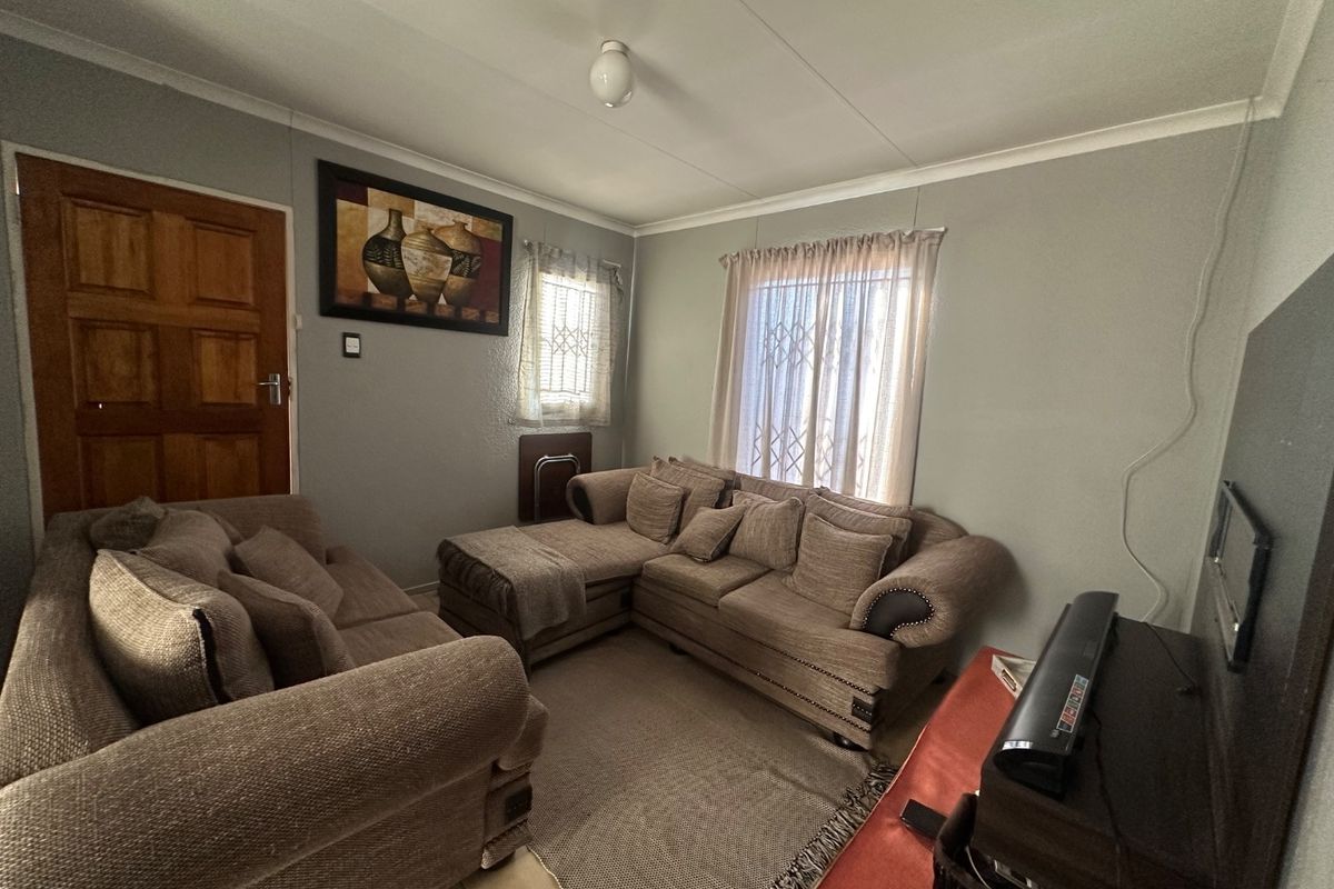 A functional living room featuring neutral wall tones, security gates on windows, and a solid timber entrance door.