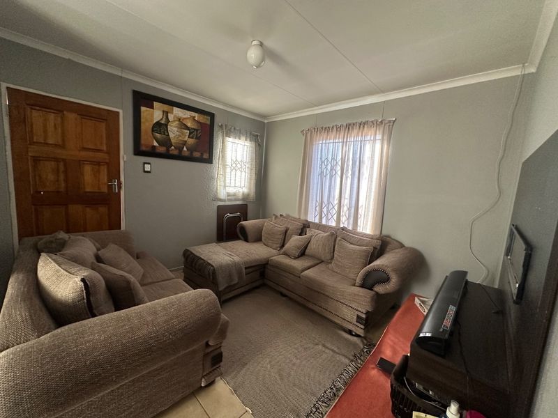 A functional living room featuring neutral wall tones, security gates on windows, and a solid timber entrance door.