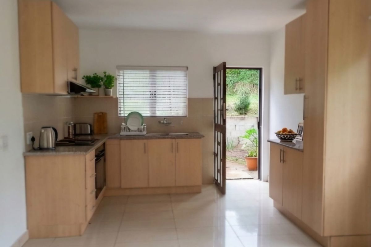 A functional kitchen featuring light wood cabinetry, granite countertops, built-in appliances, and direct access to an outdoor area through a side door.