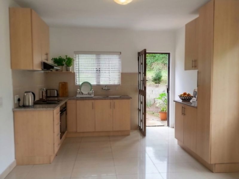 A functional kitchen featuring light wood cabinetry, granite countertops, built-in appliances, and direct access to an outdoor area through a side door.