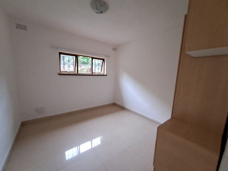 An empty bedroom featuring tiled flooring, a built-in cupboard, and a window fitted with security bars.