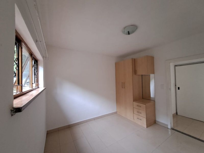 A simple bedroom featuring tiled flooring, a built-in wardrobe with integrated vanity, and a window with security bars.