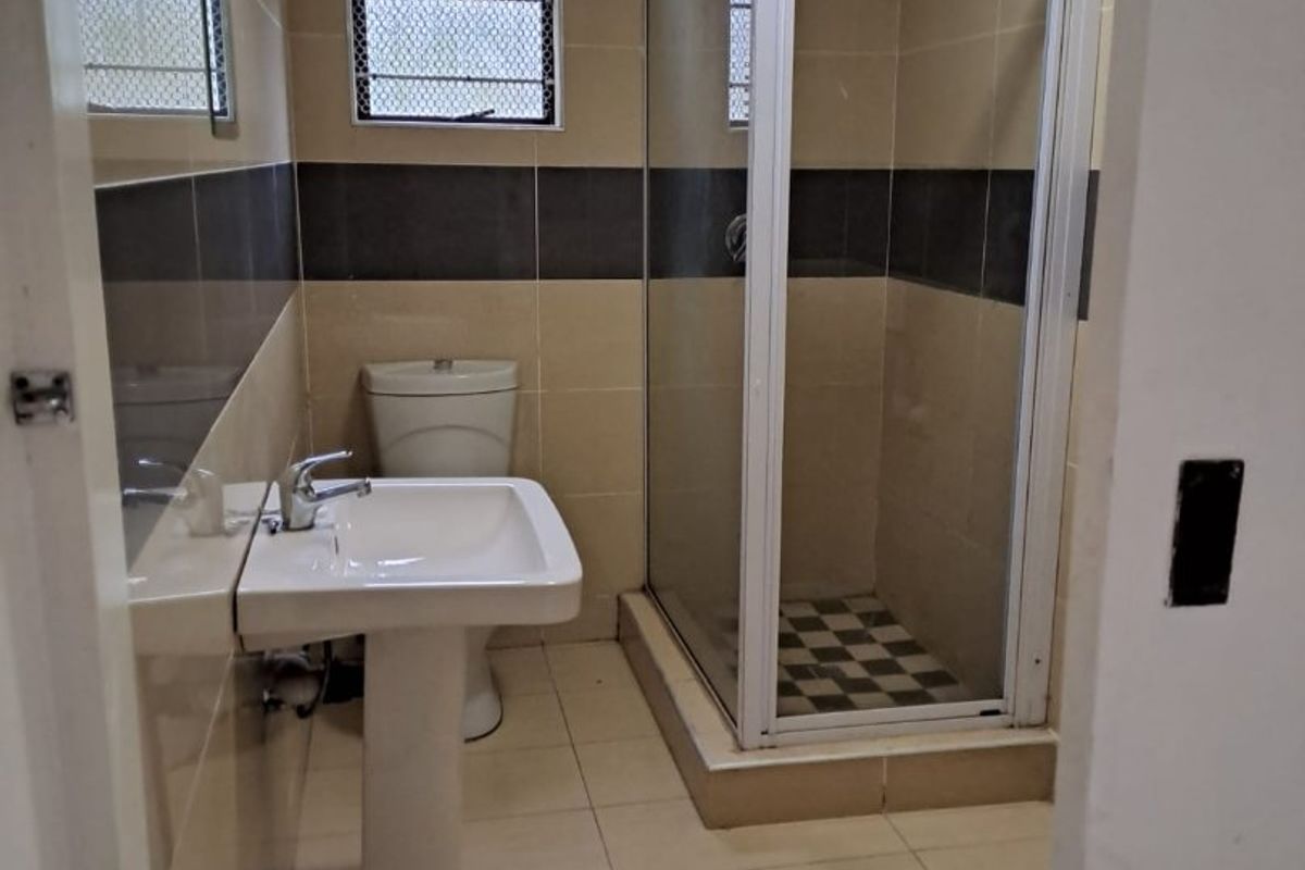 A functional bathroom featuring a pedestal washbasin, a toilet, and a glass-enclosed shower with neutral wall and floor tiling.
