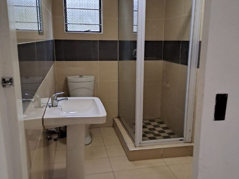 A functional bathroom featuring a pedestal washbasin, a toilet, and a glass-enclosed shower with neutral wall and floor tiling.