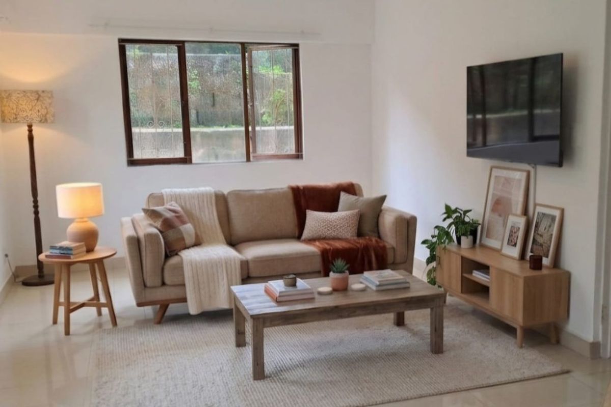 A bright and well-maintained living room featuring neutral tiled flooring and a large casement window providing natural light.