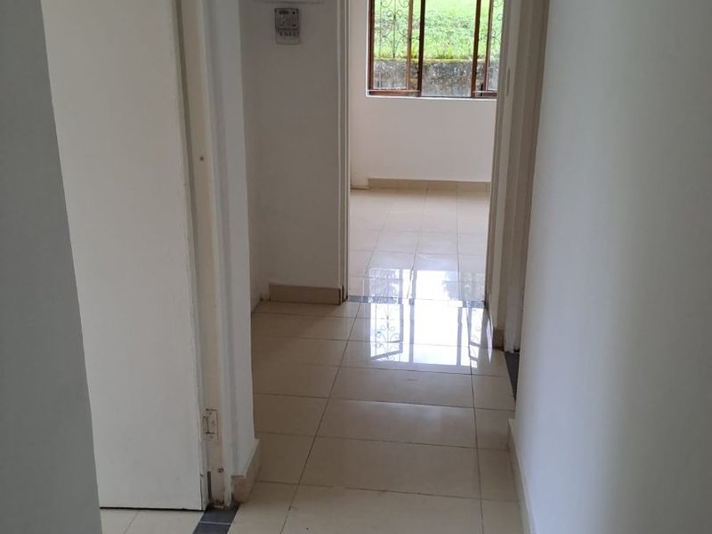 A bright, empty hallway featuring neutral tiled flooring, leading through to an adjacent room with natural light and security window bars.