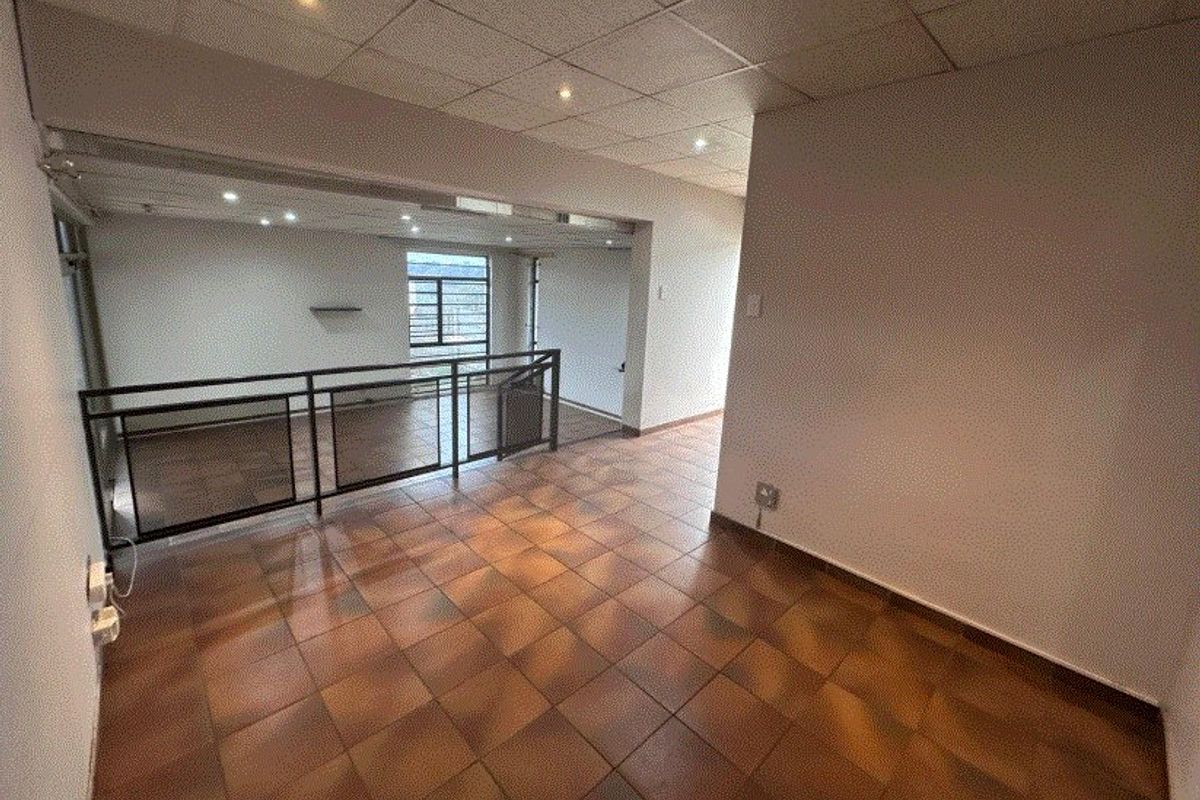 An empty, open-plan living area featuring tiled flooring, a suspended ceiling with recessed lighting, and a metal balustrade overlooking the lower level.