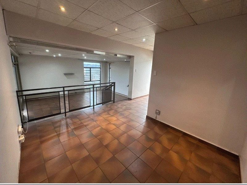 An empty, open-plan living area featuring tiled flooring, a suspended ceiling with recessed lighting, and a metal balustrade overlooking the lower level.