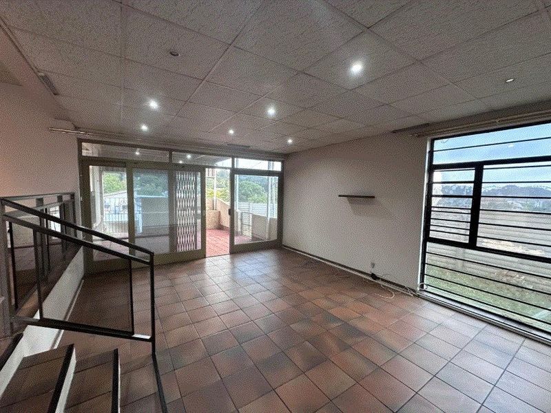 Spacious, empty living area featuring tiled flooring, a drop ceiling with recessed lighting, and large sliding doors leading to an outdoor patio space.