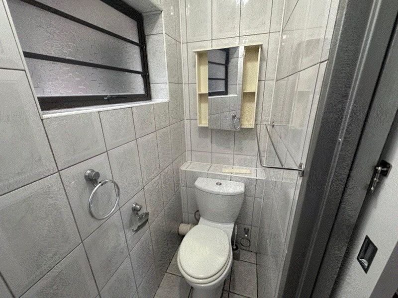 A compact, fully tiled guest bathroom featuring a standard toilet, wall-mounted mirror cabinet, and an obscured glass window for privacy.