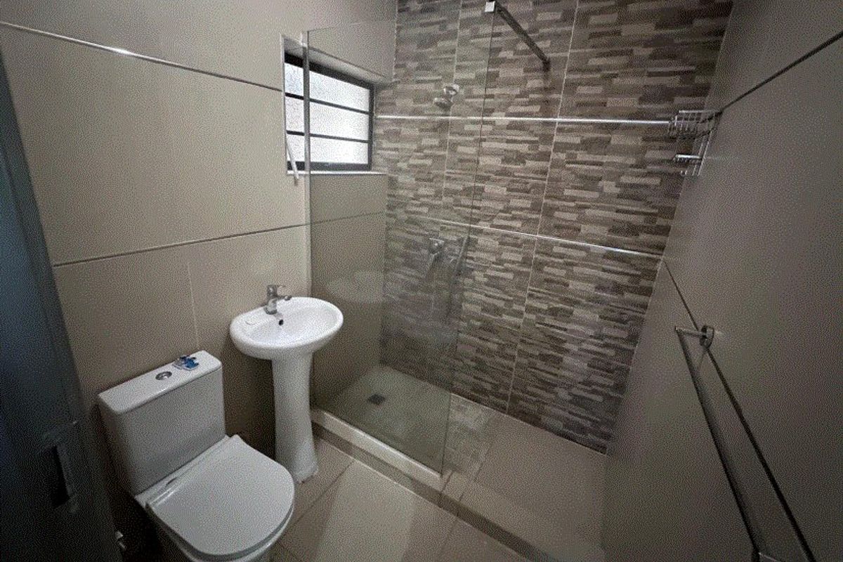 Modern bathroom featuring a pedestal basin, toilet, and a walk-in shower with a glass screen and decorative tiled accent wall.