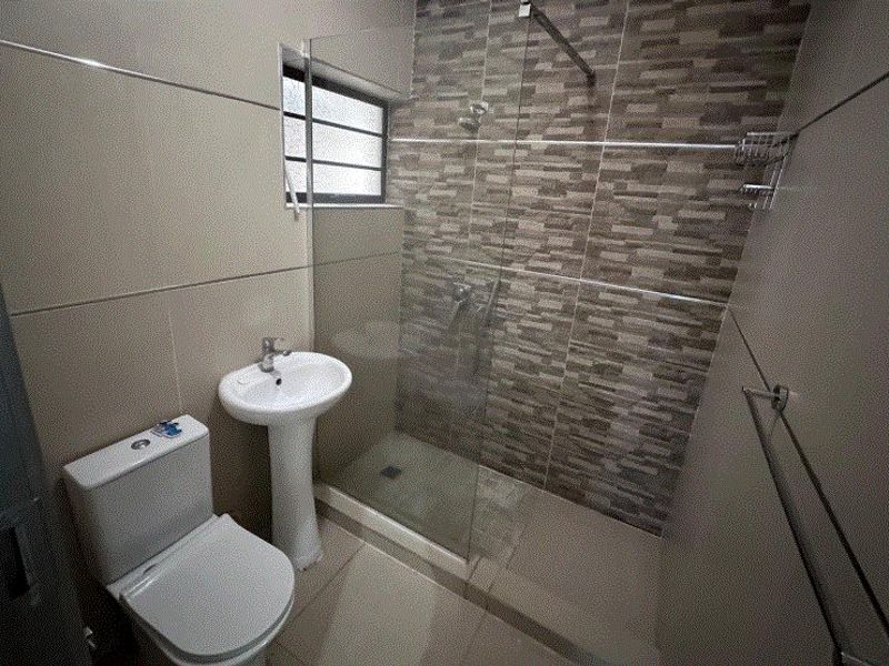 Modern bathroom featuring a pedestal basin, toilet, and a walk-in shower with a glass screen and decorative tiled accent wall.