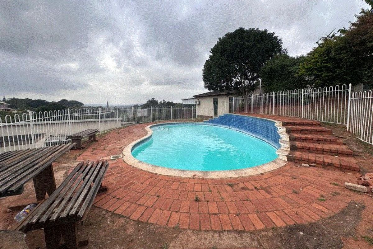 Outdoor pool area featuring a kidney-shaped swimming pool, brick paving, and metal perimeter fencing, requiring maintenance to the surrounding brickwork and paving surfaces.