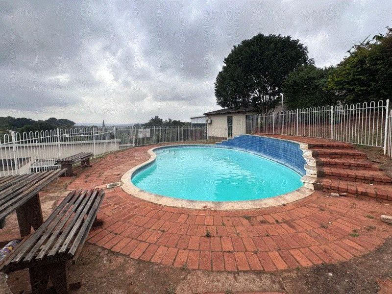 Outdoor pool area featuring a kidney-shaped swimming pool, brick paving, and metal perimeter fencing, requiring maintenance to the surrounding brickwork and paving surfaces.