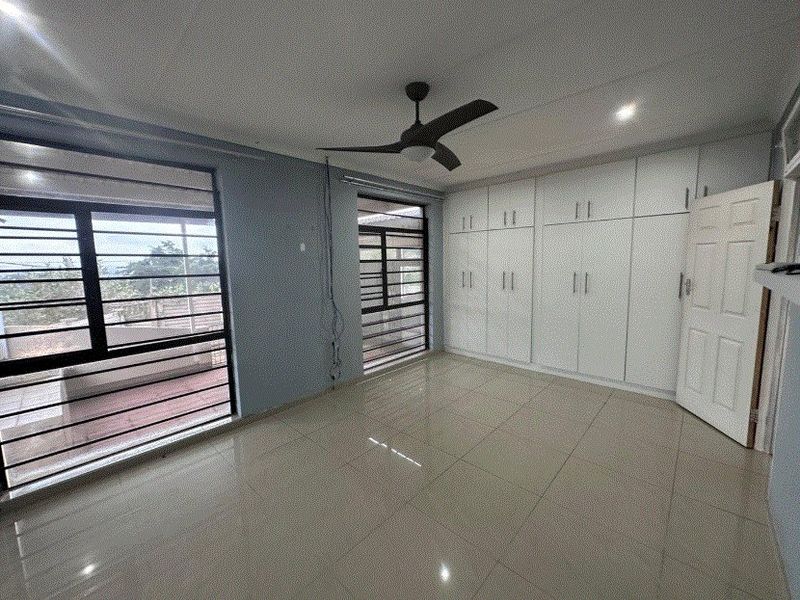 Spacious bedroom featuring neutral tiled flooring, extensive built-in cabinetry, a ceiling fan, and large windows with security bars.