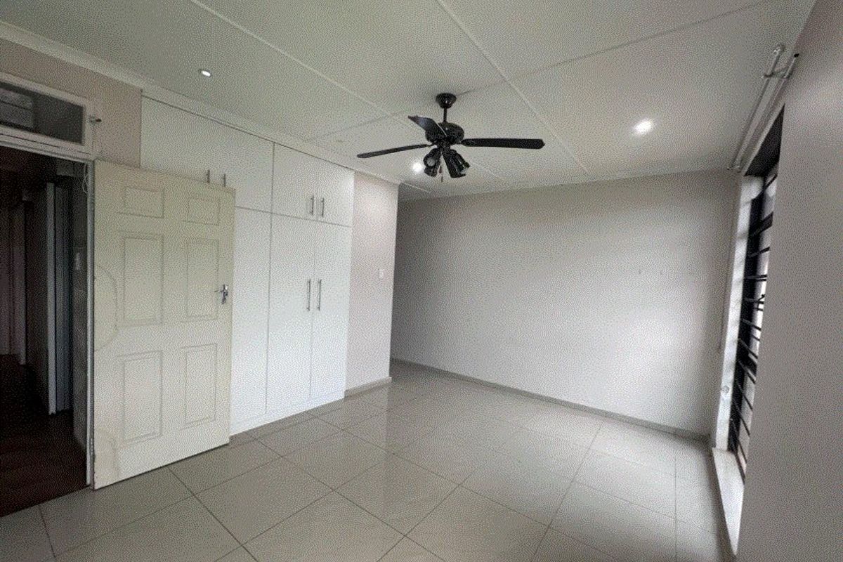 A clean, empty bedroom featuring neutral tiled flooring, built-in cupboards, a ceiling fan, and recessed lighting, offering a blank canvas for personalization.